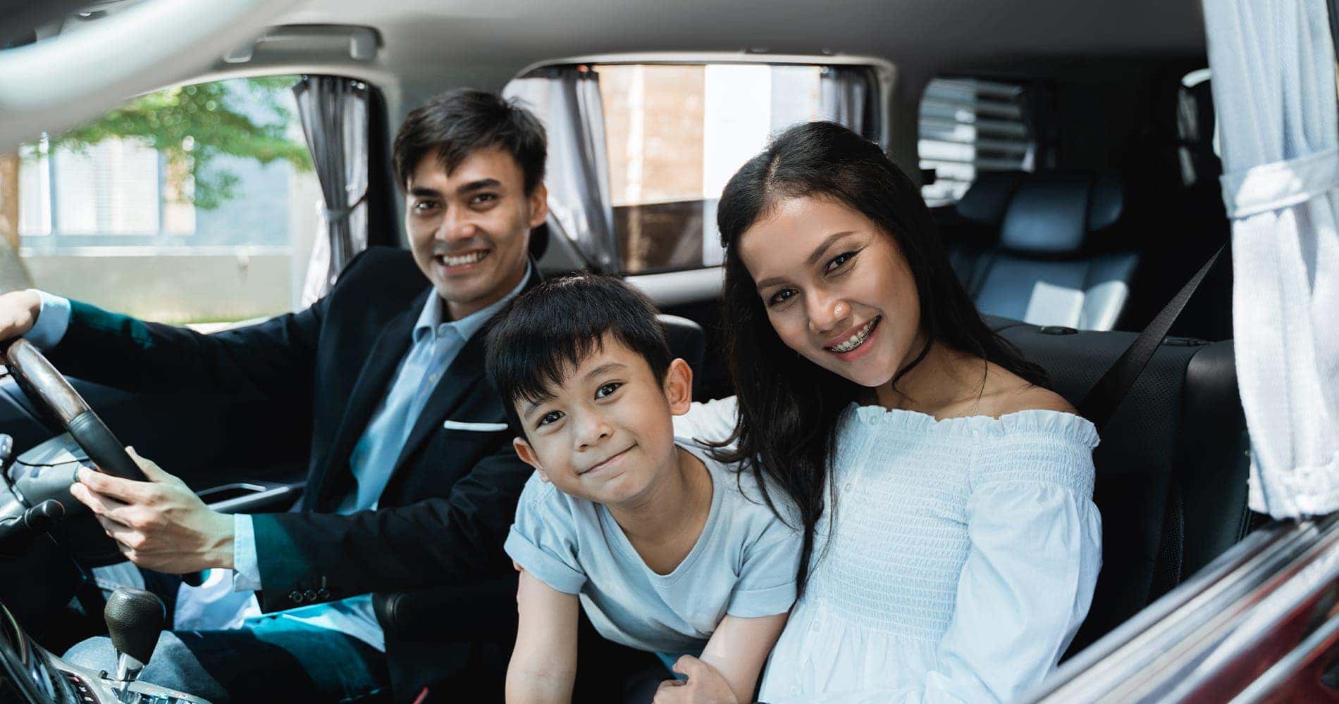 Family smiling in a car, with a man driving, a woman, and a young boy in the back seat.
