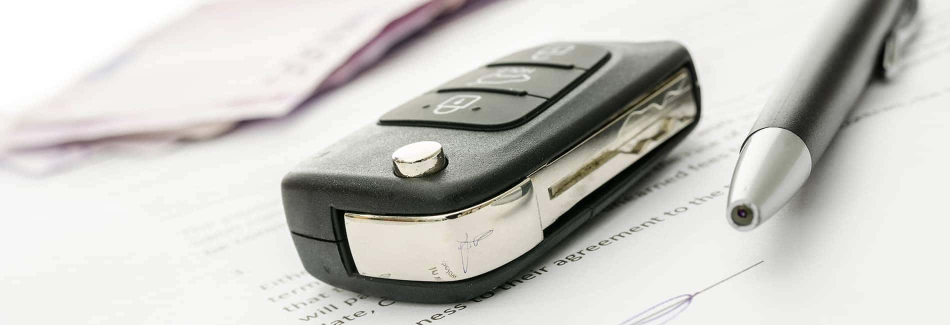 Car key and pen on a document, suggesting a vehicle agreement or contract.