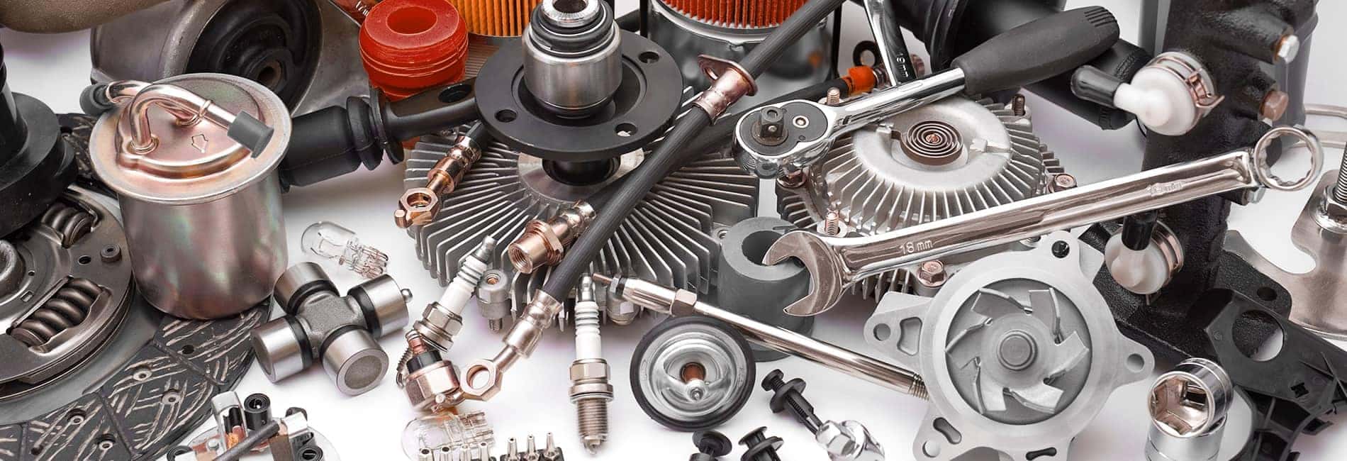 Assorted automotive parts including gears, spark plugs, and wrenches scattered on a white surface.