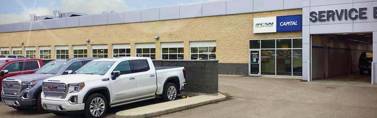 Pickup trucks parked outside an automotive service center with signage on the building.