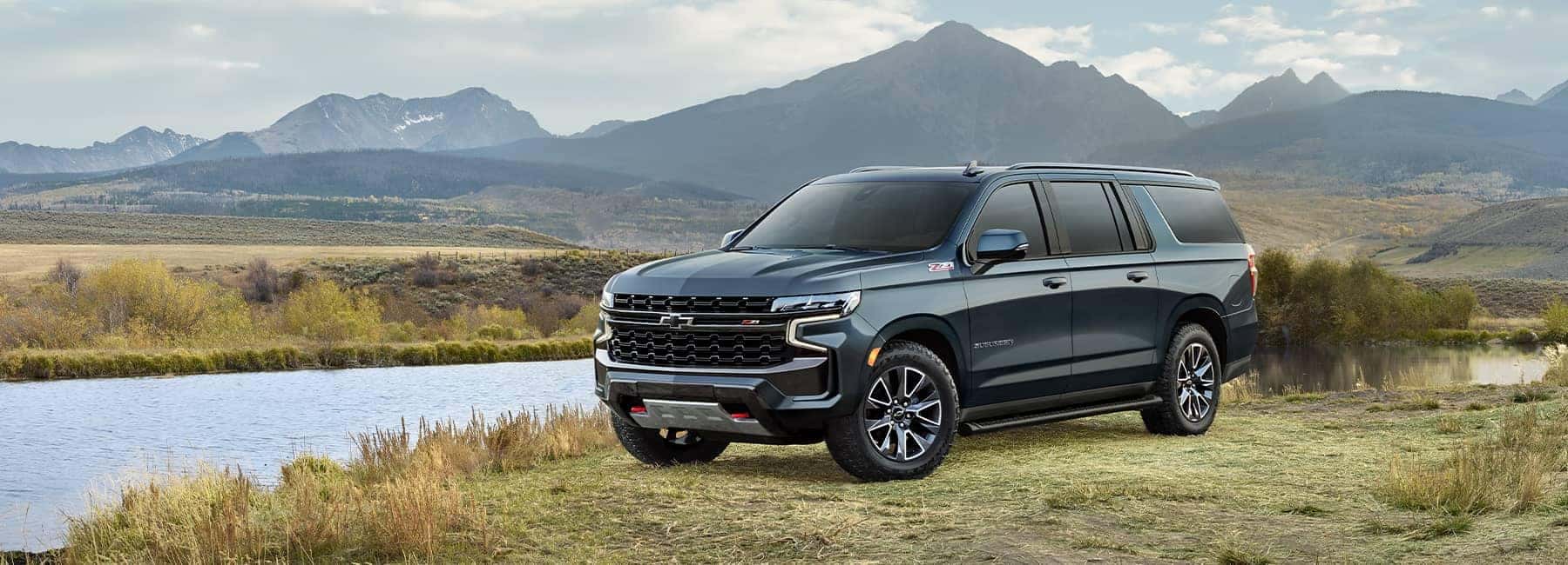 SUV parked beside a scenic lake with mountains in the background, highlighting outdoor adventure.