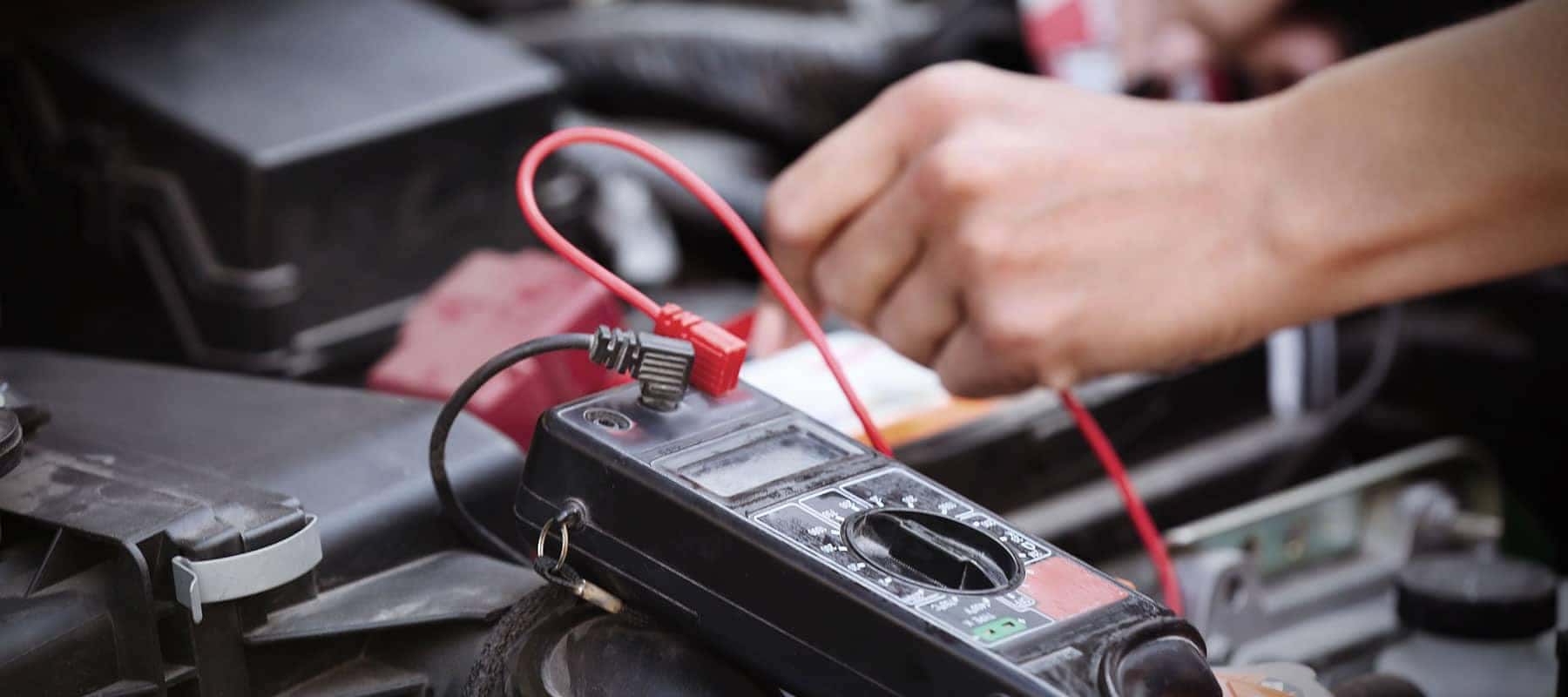 Hands using a multimeter for car diagnostics, measuring electronic components.