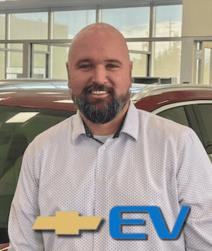 Man in a jacket stands in front of a white car, with a Chevrolet logo and "EV" text overlay.