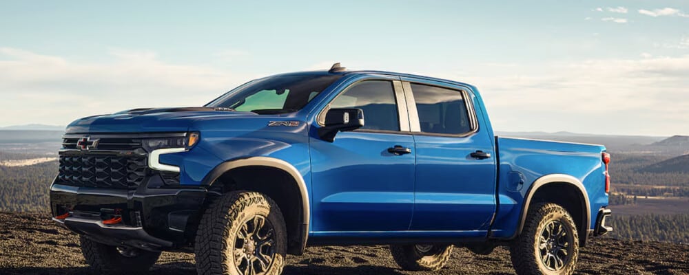 Blue pickup truck on a rocky landscape with distant mountains and a clear sky.