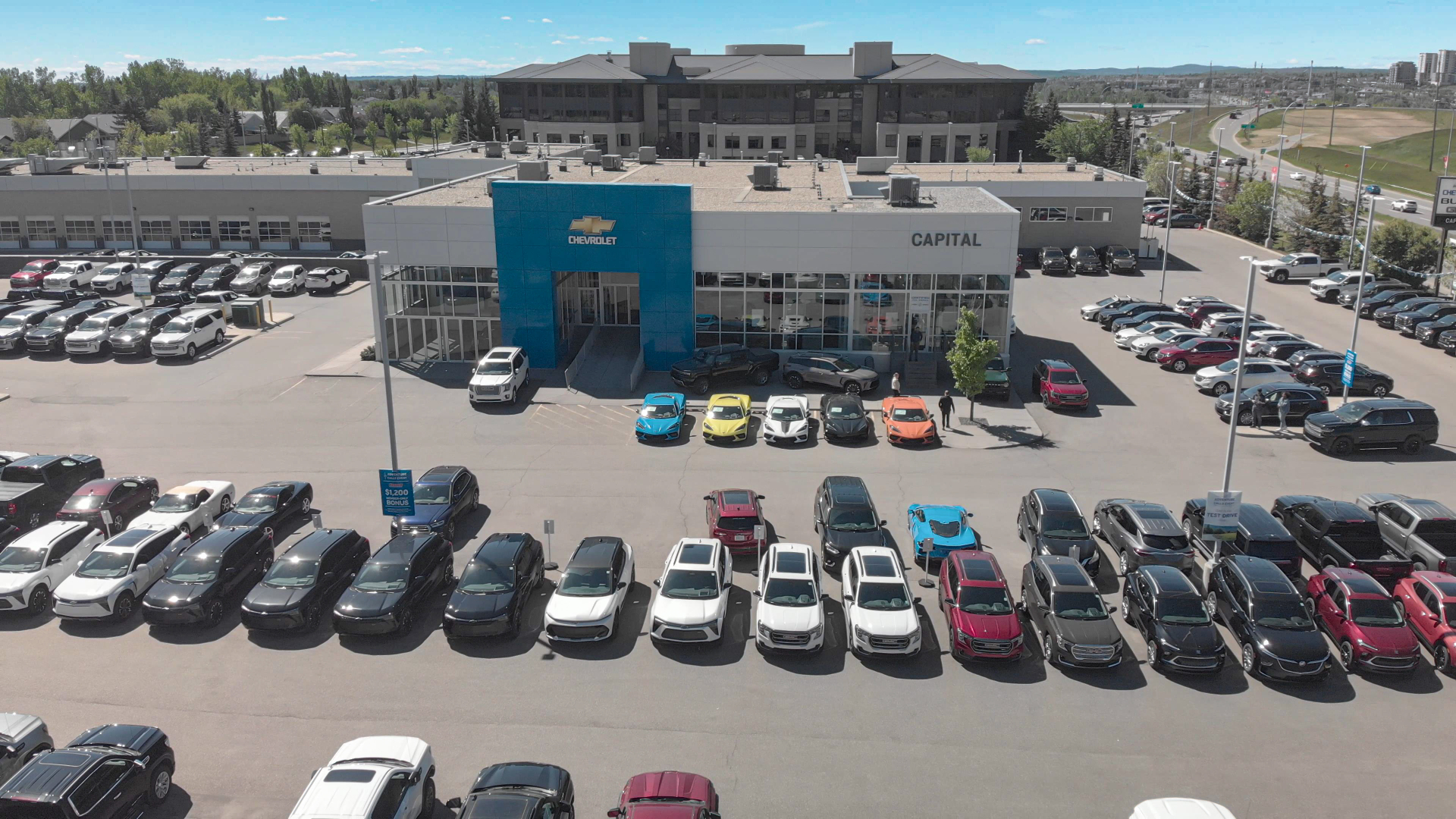 Aerial view of a Chevrolet car dealership with numerous cars parked outside, under a clear blue sky.